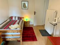 Zimmerbeispiel mit Bett, Nachttisch, rotem Teppichläufer und Wandbild